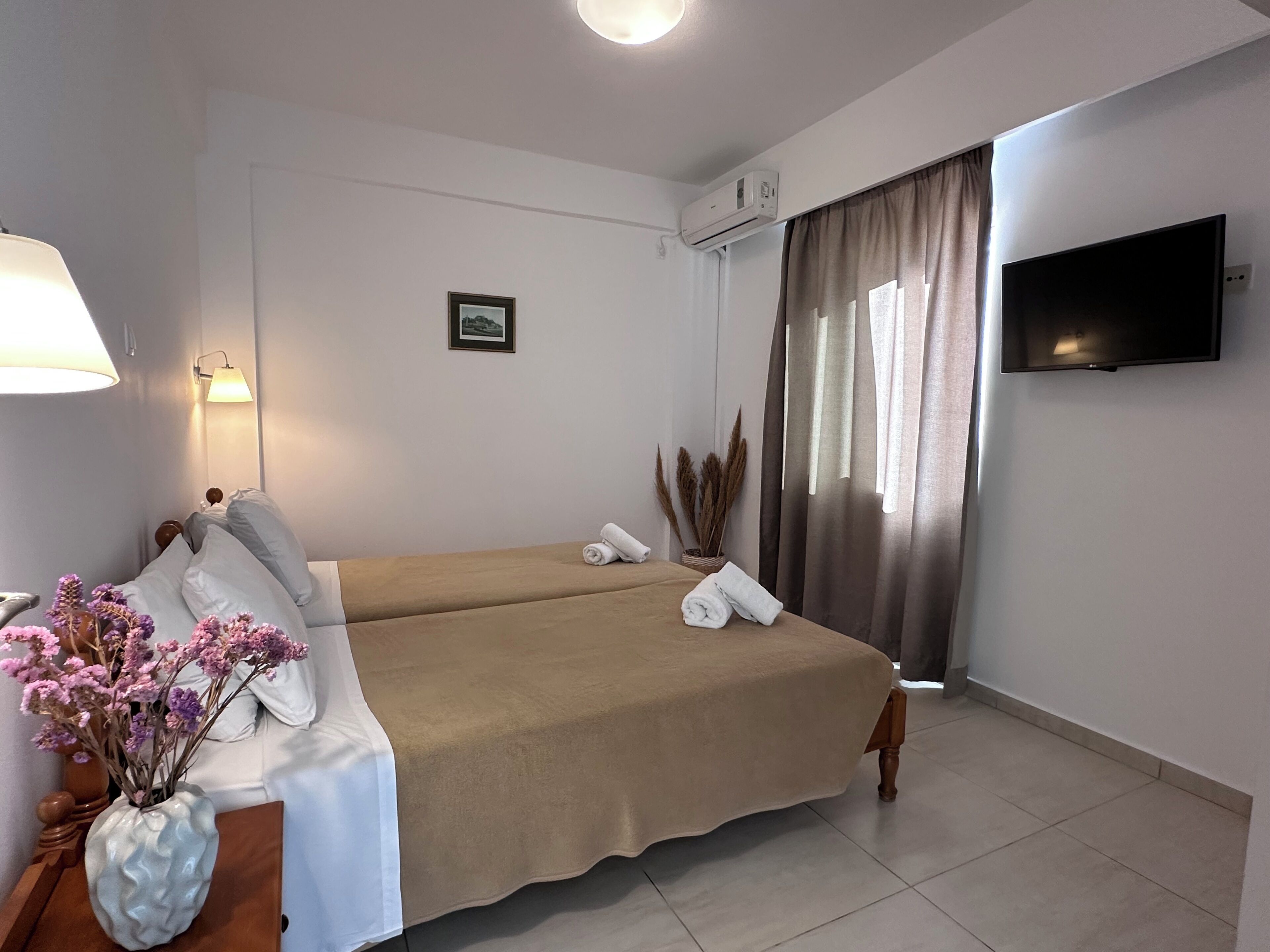 A hotel room with a bed, a TV, a lamp, and a vase with flowers.