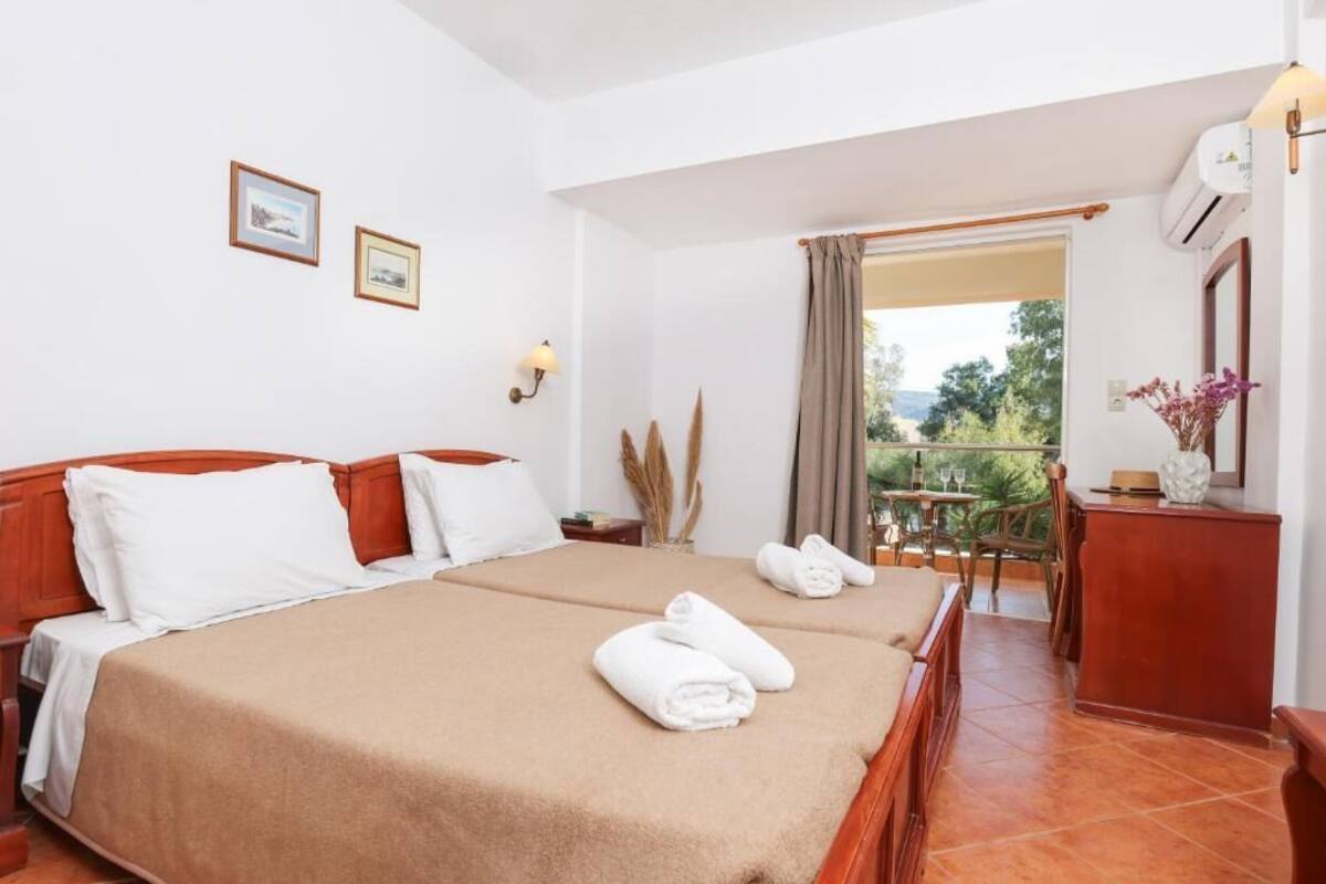 A hotel room with a double bed, a desk, a chair, and a balcony with a view.