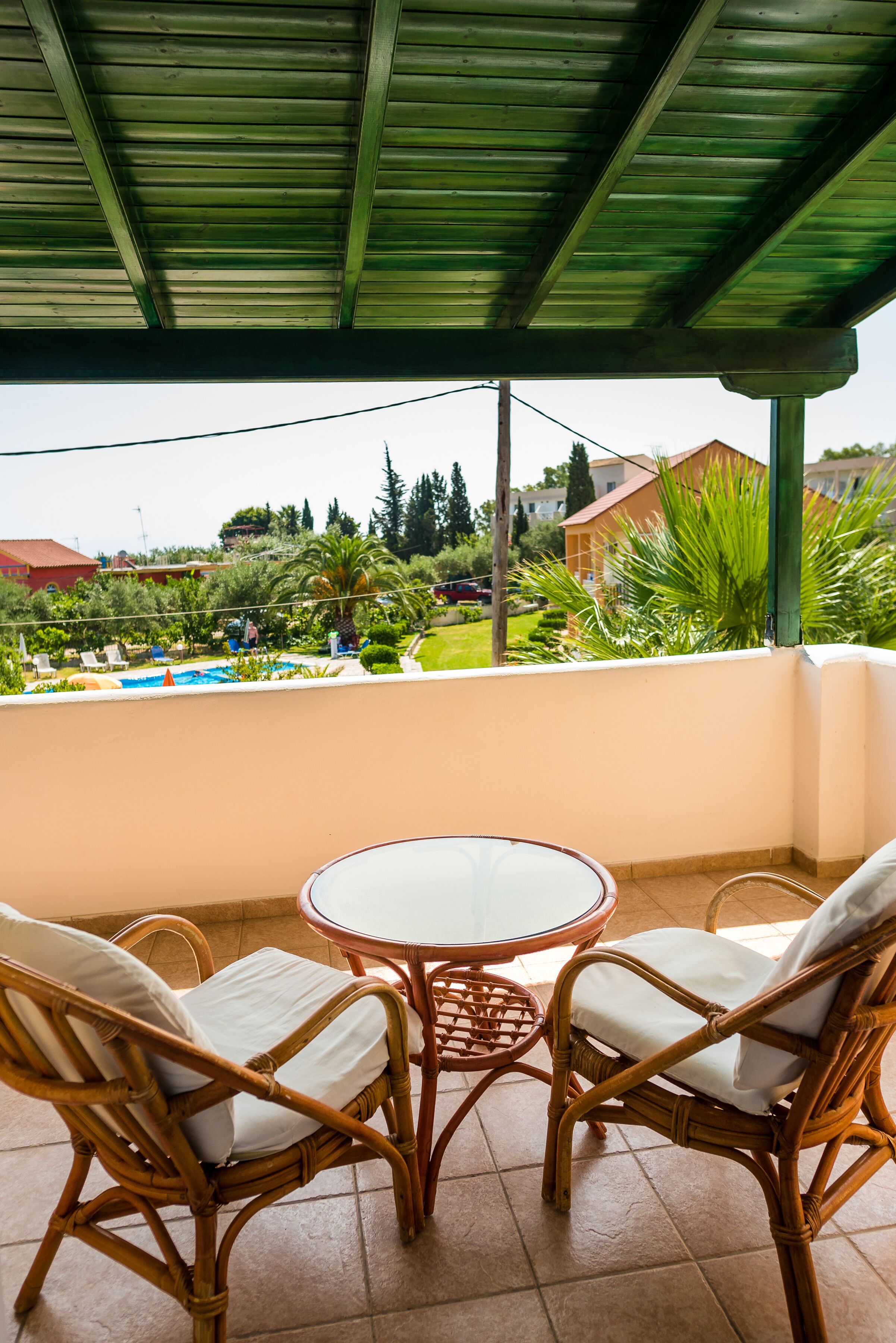 A covered patio with wicker furniture and a view of a swimming pool and greenery.