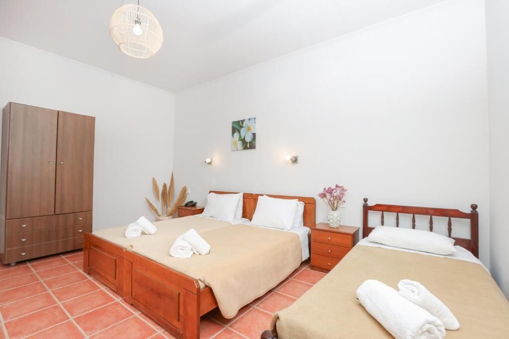 Une chambre d’hôtel avec deux lits, une armoire, une table de chevet avec une lampe et un luminaire fixé au mur.