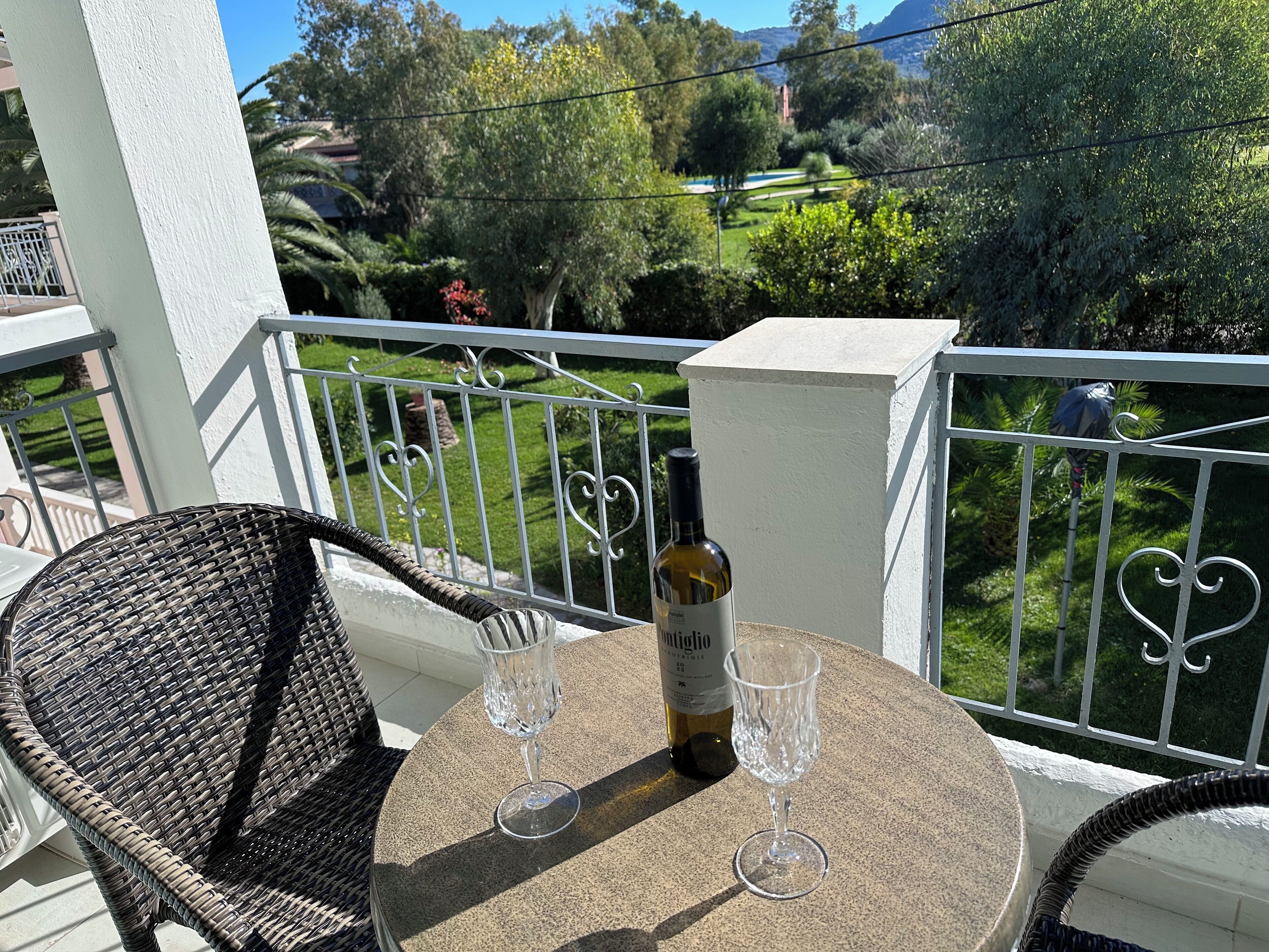 Ein Balkon mit rundem Tisch, zwei Weingläsern und einer Weinflasche.