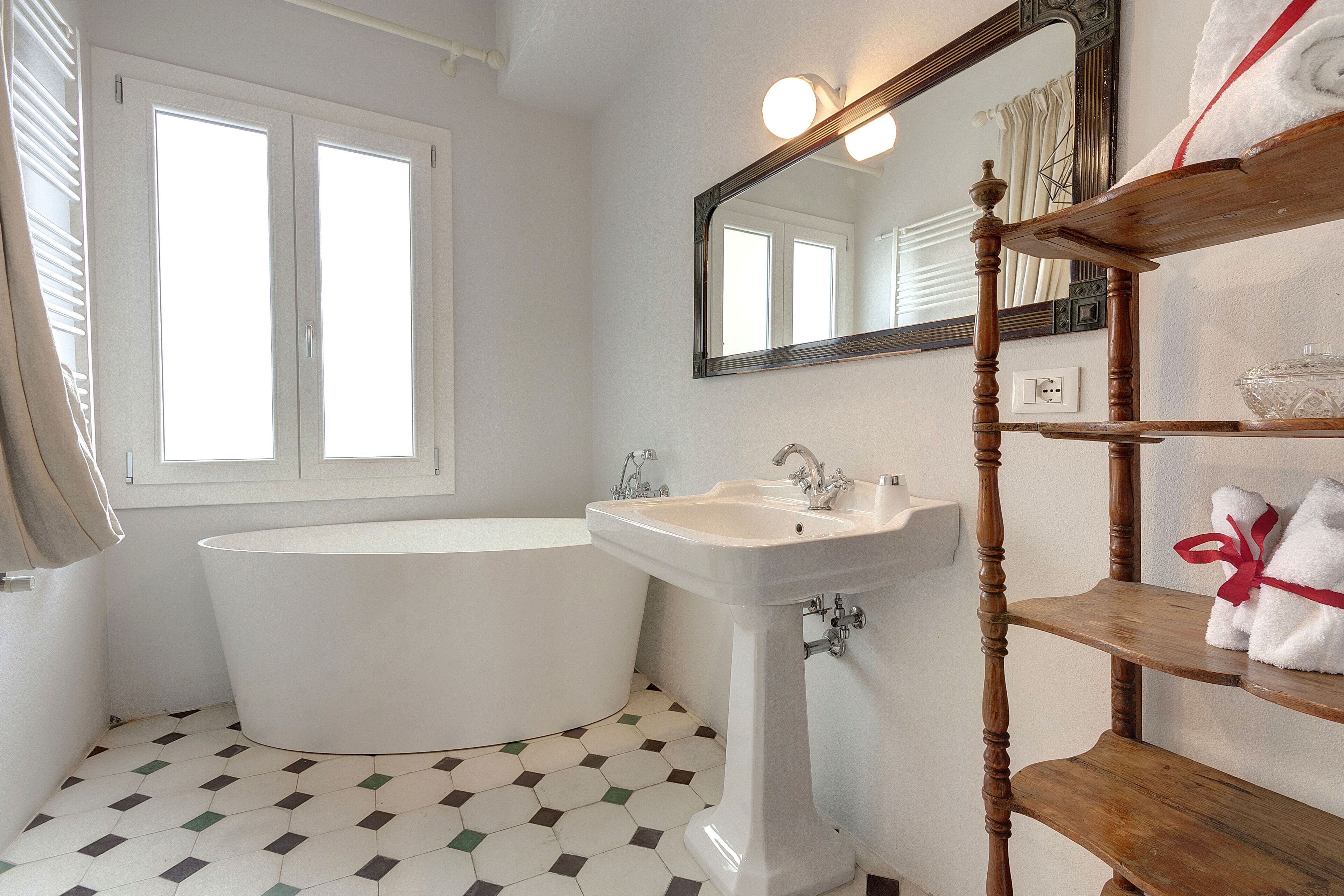 A bathroom with a bathtub, a sink, a mirror, and a shelf with towels.
