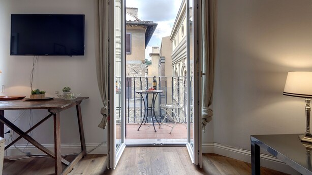 Una habitación con televisión montada en la pared, una mesa con lámpara y vistas al balcón exterior.