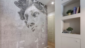 A hallway with a textured wall, a door, and a shelf with books and a plant. - Mamo Florence - Ricasoli Apartment (Florence)