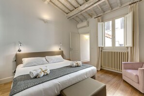A bedroom with a large bed, bedside lamps, a radiator, a window with curtains, and a pink chair. - Mamo Florence - Tegolaio Apartment (Florence)