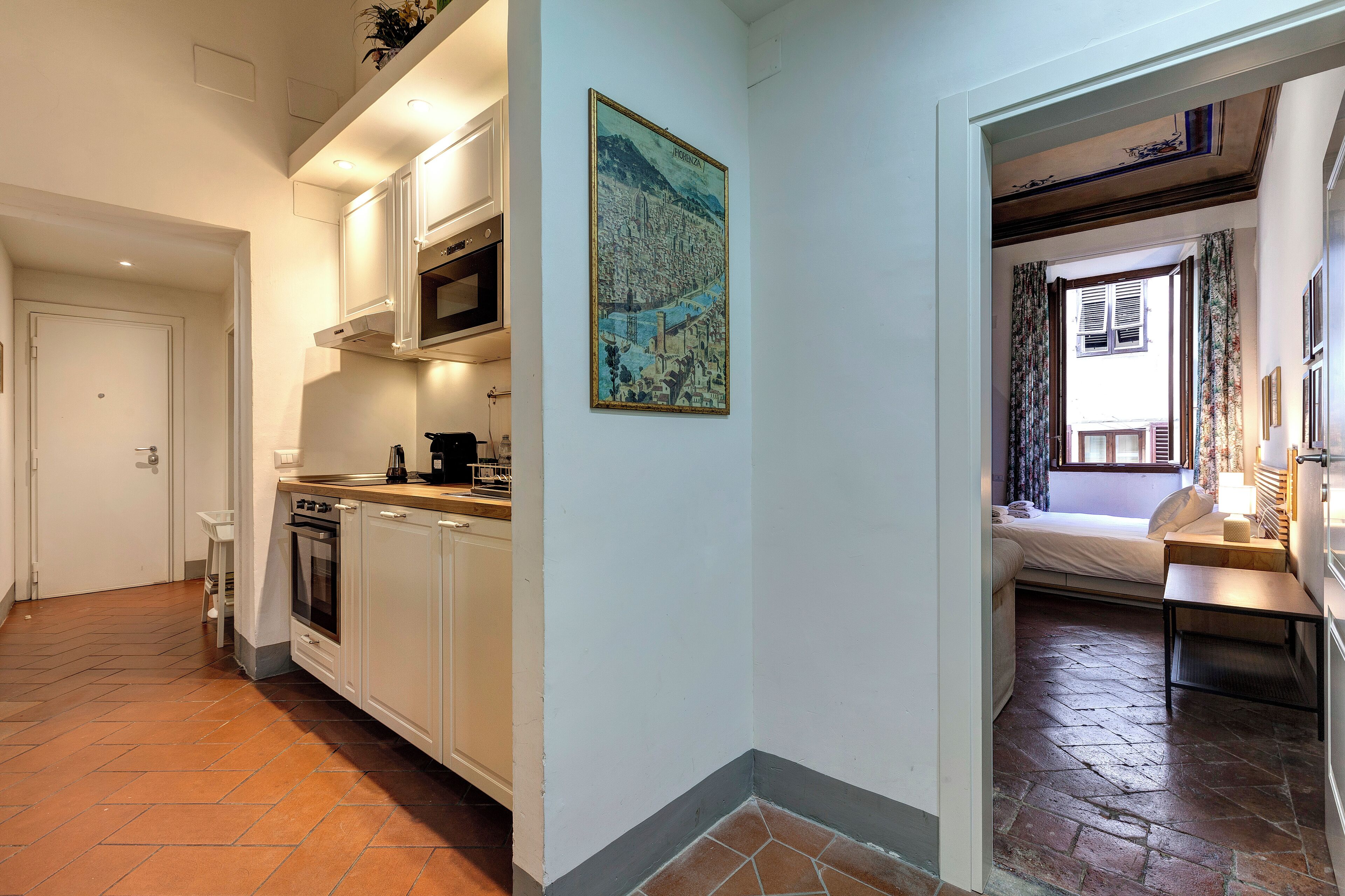 A compact kitchen with white cabinets, a microwave, and a stove. A large cityscape painting adorns the wall.
