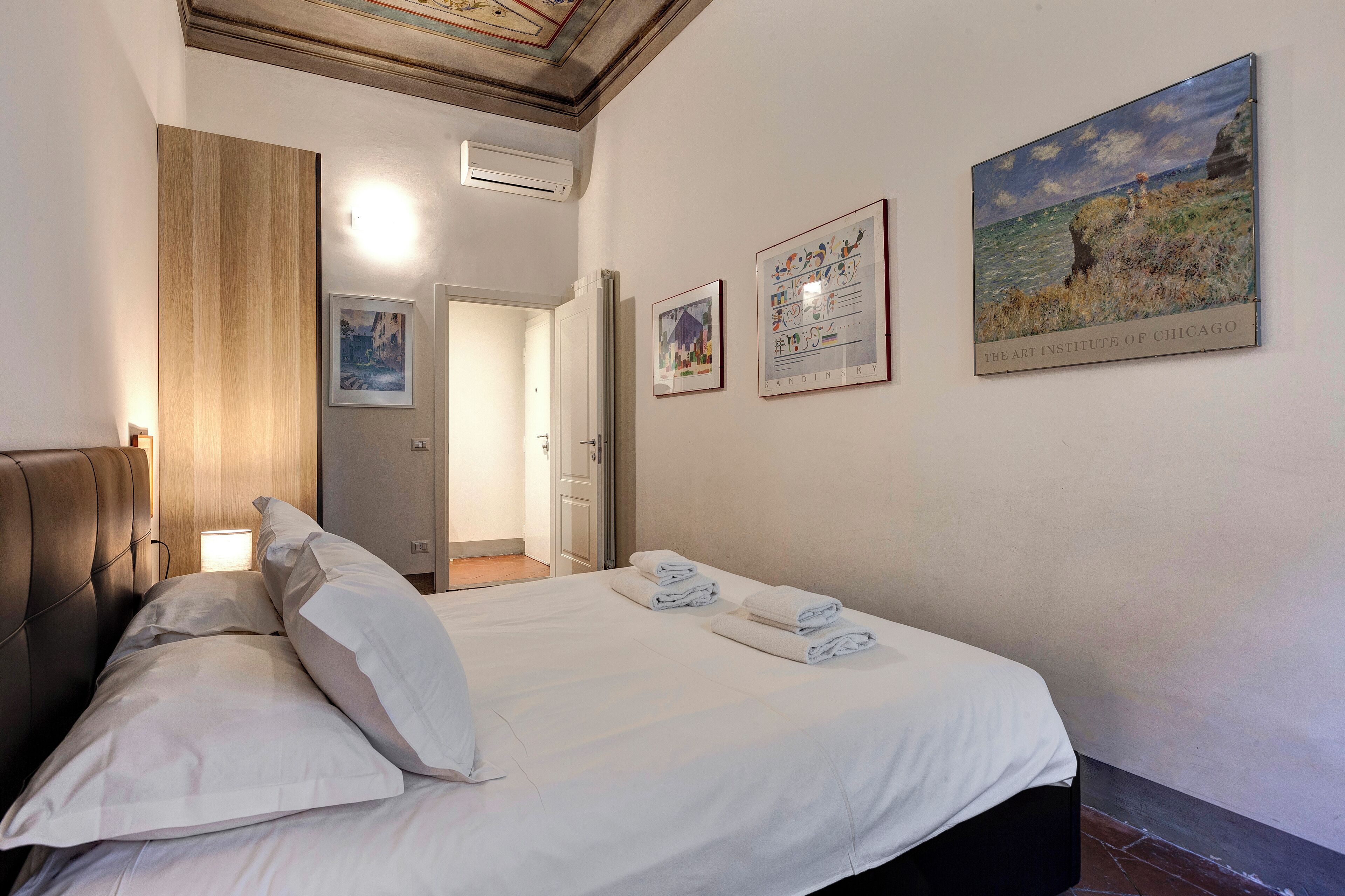 A hotel room with a bed, white linens, a wooden headboard, and artwork on the walls.
