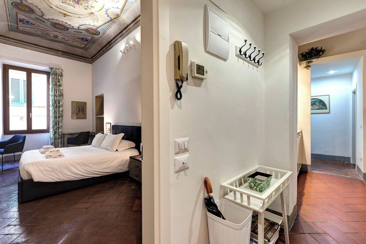 Une chambre d’hôtel comprenant un lit, un bureau, une chaise, un téléphone fixé au mur, un thermostat et une petite table avec un panier.