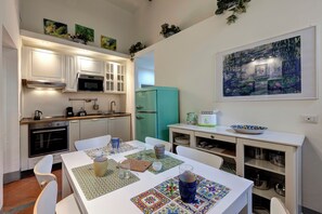A compact kitchen with white cabinets, a teal refrigerator, and a dining area with a table set for two. - Mamo Florence - Tegolaio Apartment (Florence)