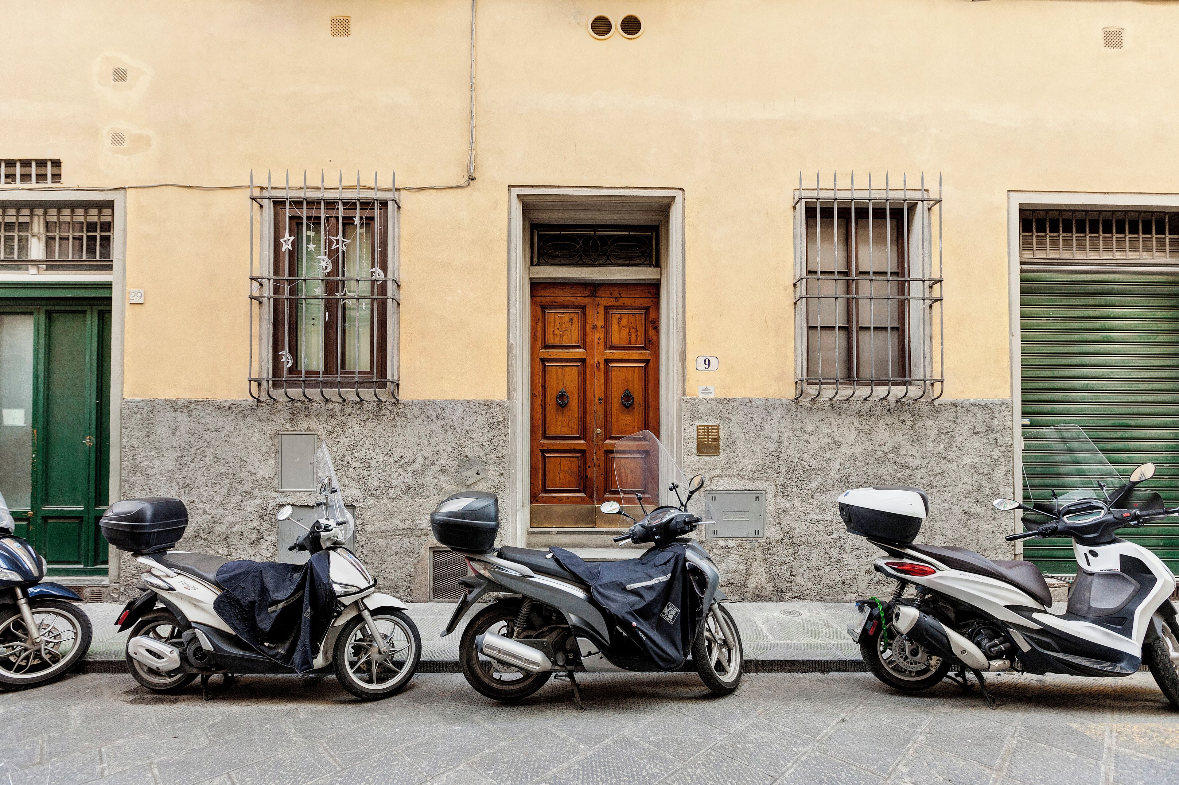 A row of parked scooters in front of a building with a green door and barred windows.