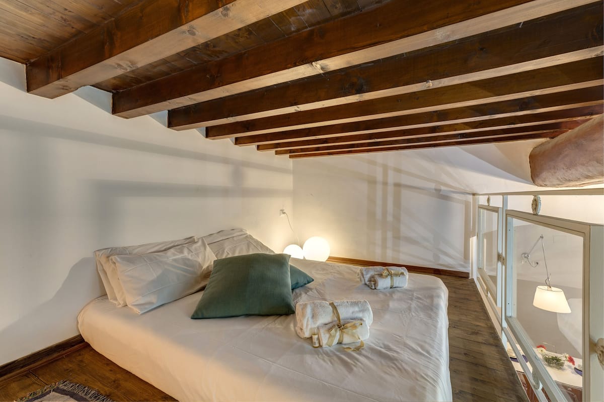 Une chambre avec un plafond en bois, un lit avec une literie blanche, un oreiller vert et deux serviettes sur le lit.