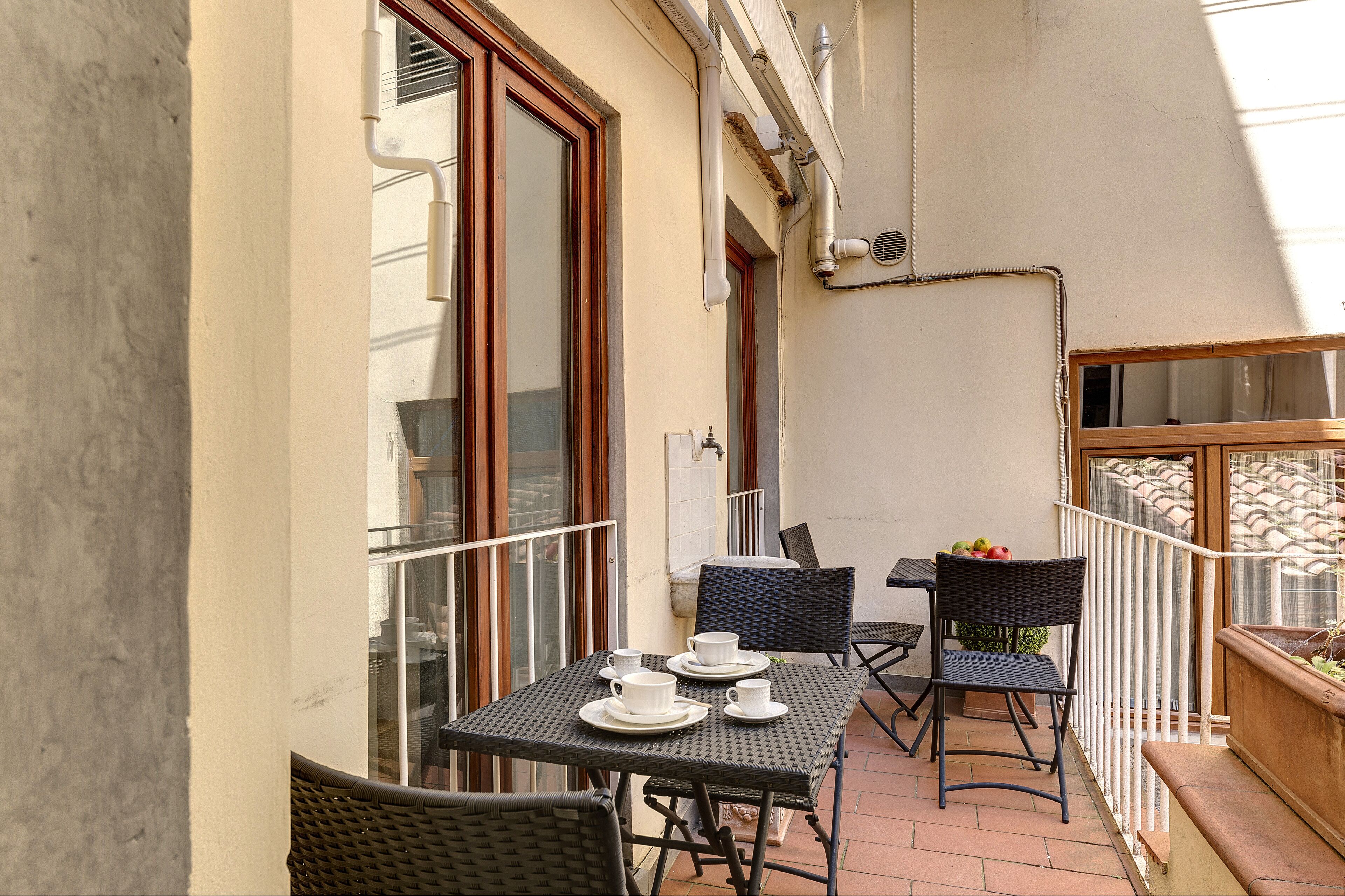 A balcony with a table set for two, two chairs, and a small plant.