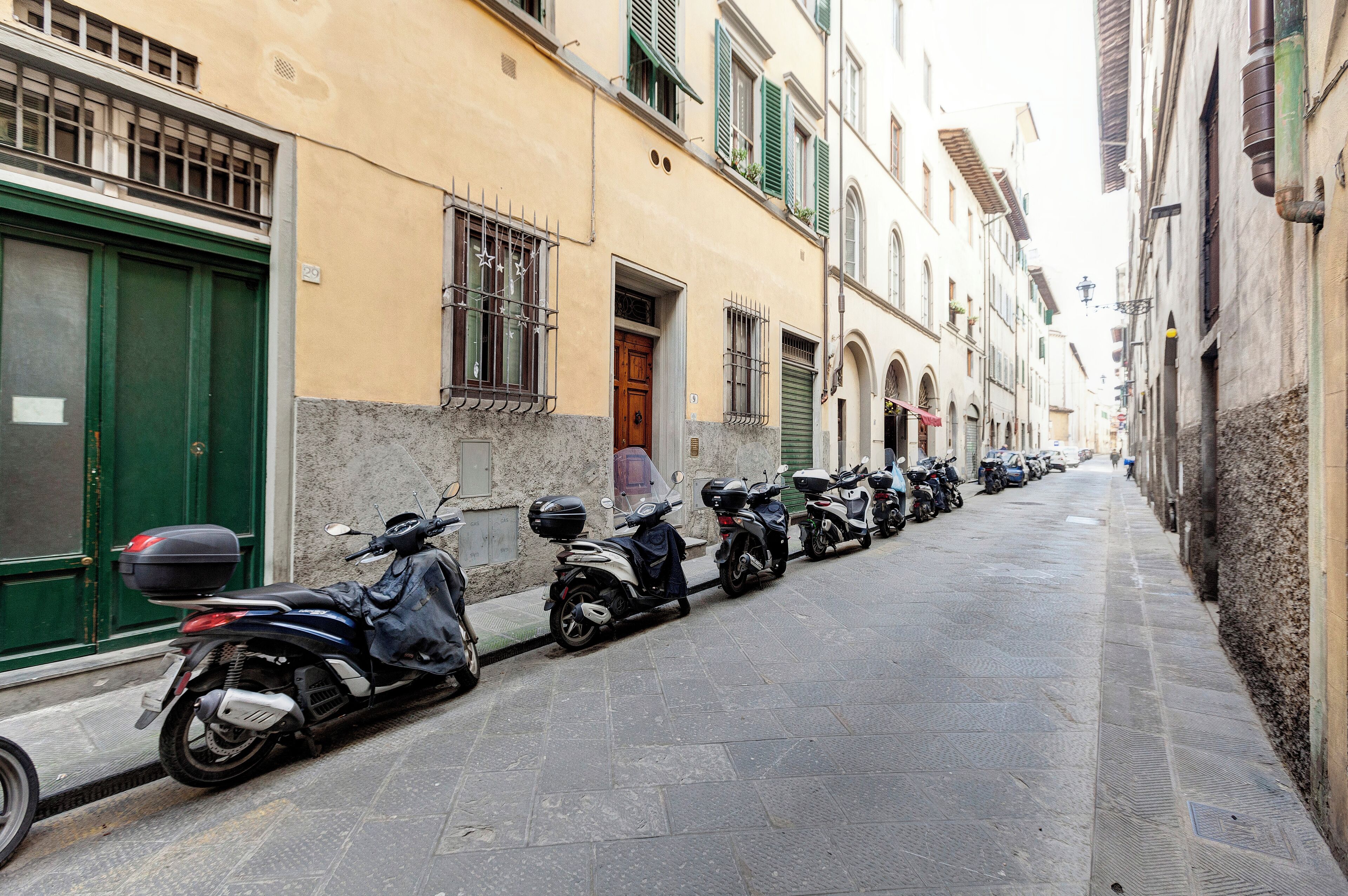 A row of parked scooters along a narrow street with buildings on either side.