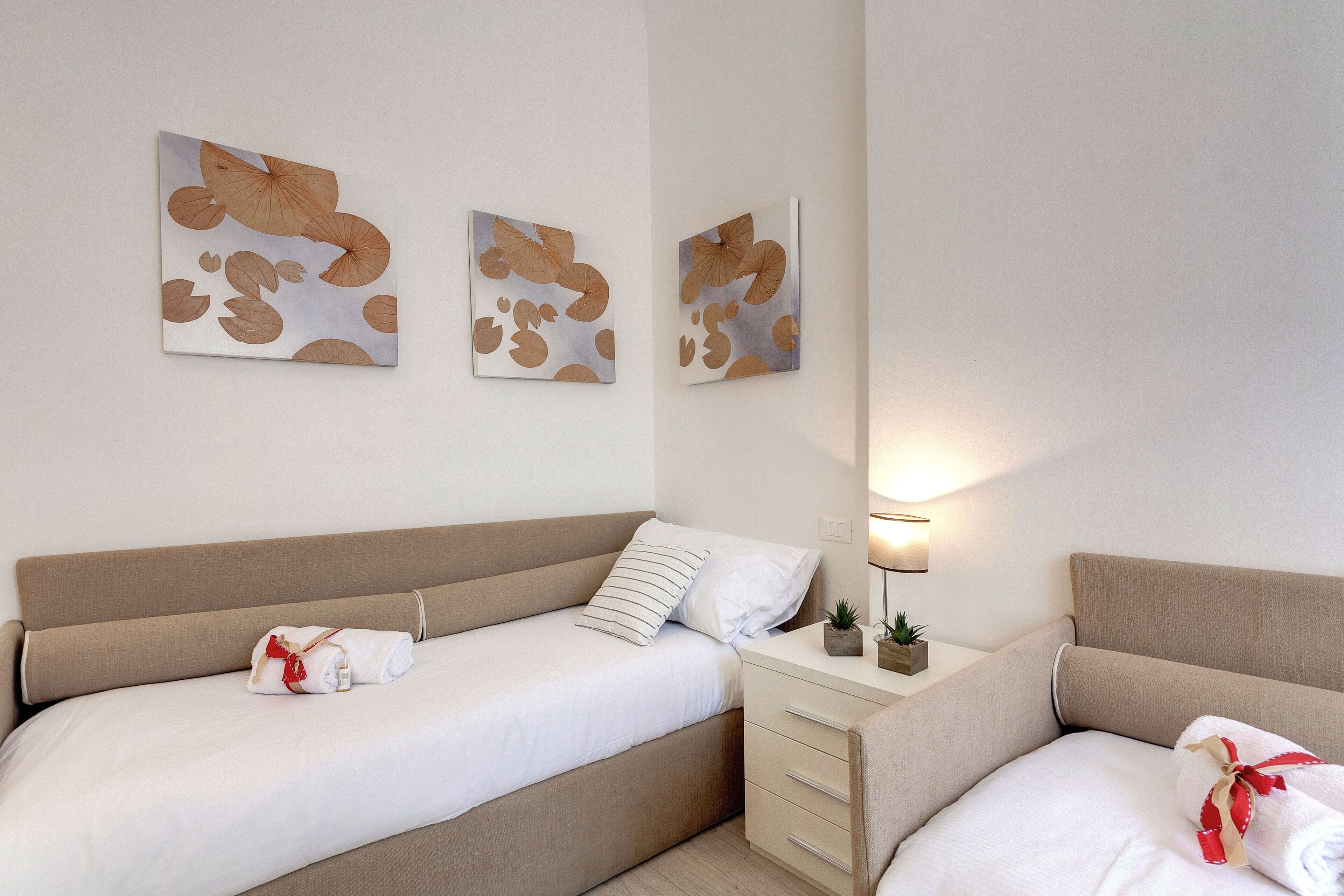 A hotel room with two beds, a bedside table with a lamp, and wall art.