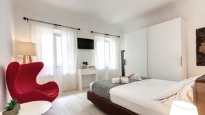 Habitación de hotel moderna con una cama grande, una silla roja, una mesita pequeña y un televisor en la pared.