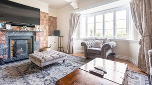A living room with a fireplace, a sofa, a coffee table, and a window with curtains. - St Anne's House, Sea Views, 7 Bedrooms - Sleeps 30 (Plymouth)