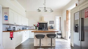 A modern kitchen with white cabinets, a central island with two bar stools, stainless steel appliances, and a visible fire blanket. - St Anne's House, Sea Views, 7 Bedrooms - Sleeps 30 (Plymouth)