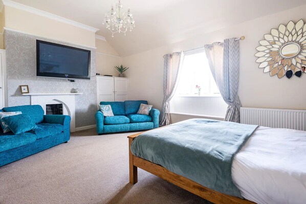A bedroom with a bed, a blue sofa, a TV, a chandelier, and a window with curtains. - St Anne's House, Sea Views, 7 Bedrooms - Sleeps 30 (Plymouth)