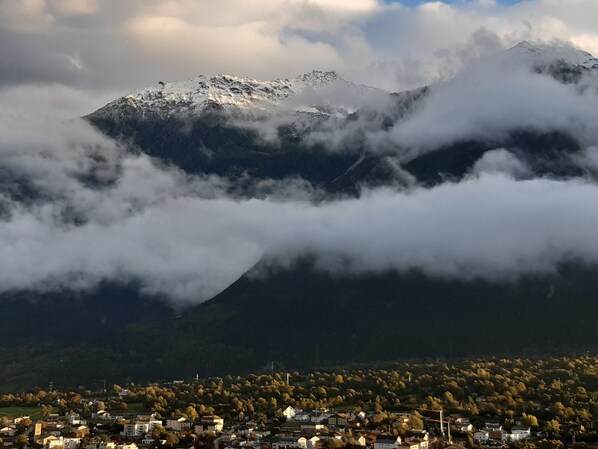 Una montaña con cumbre nevada, parcialmente cubierta por nubes, y un pueblo con edificios en la base.
