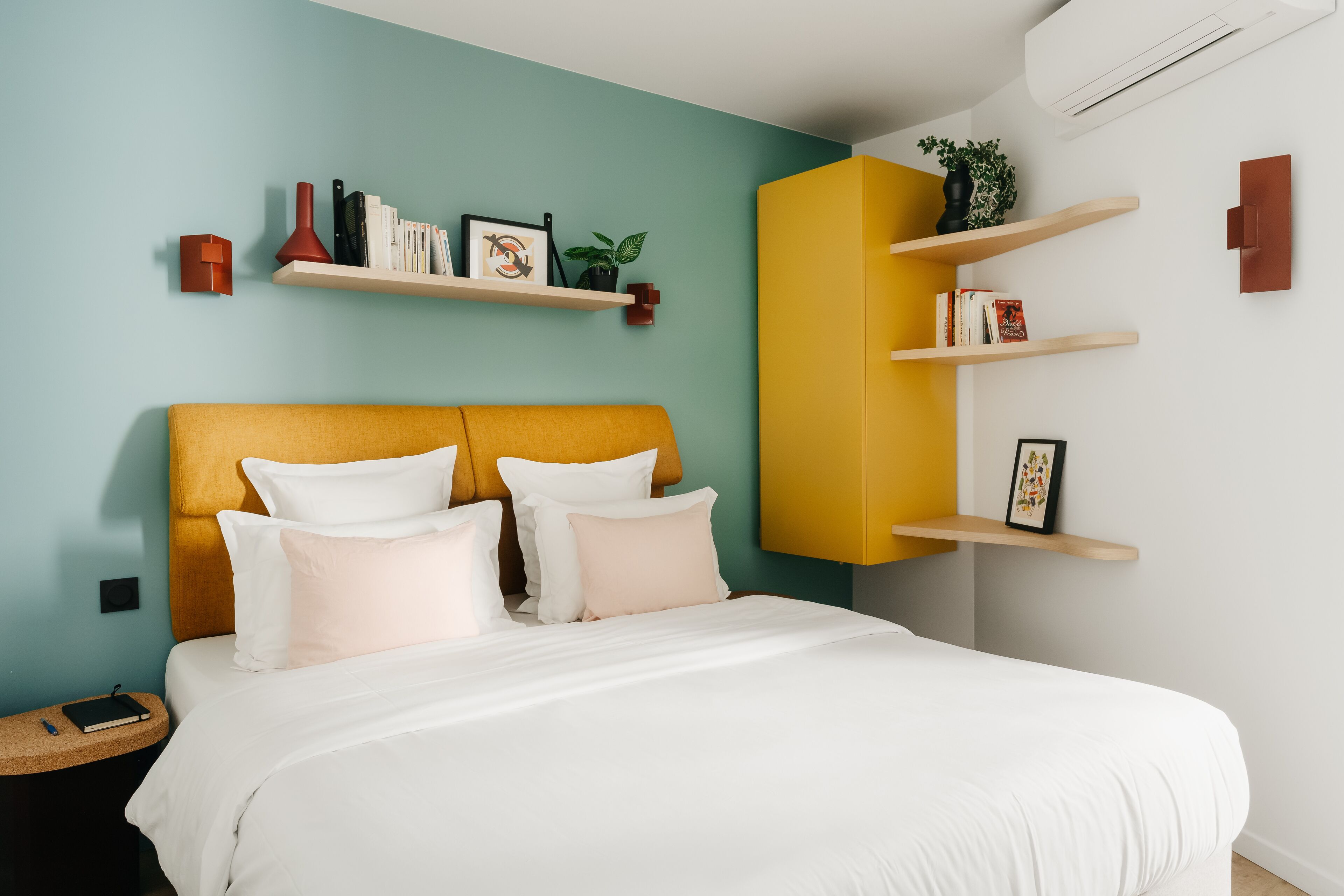 A modern bedroom with a bed, a nightstand, and a built-in shelf with books and a plant.
