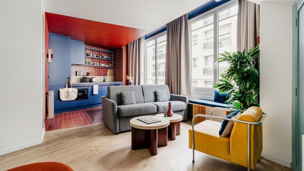 A modern living room with a sofa, two side tables, a yellow armchair, and a large window with curtains.