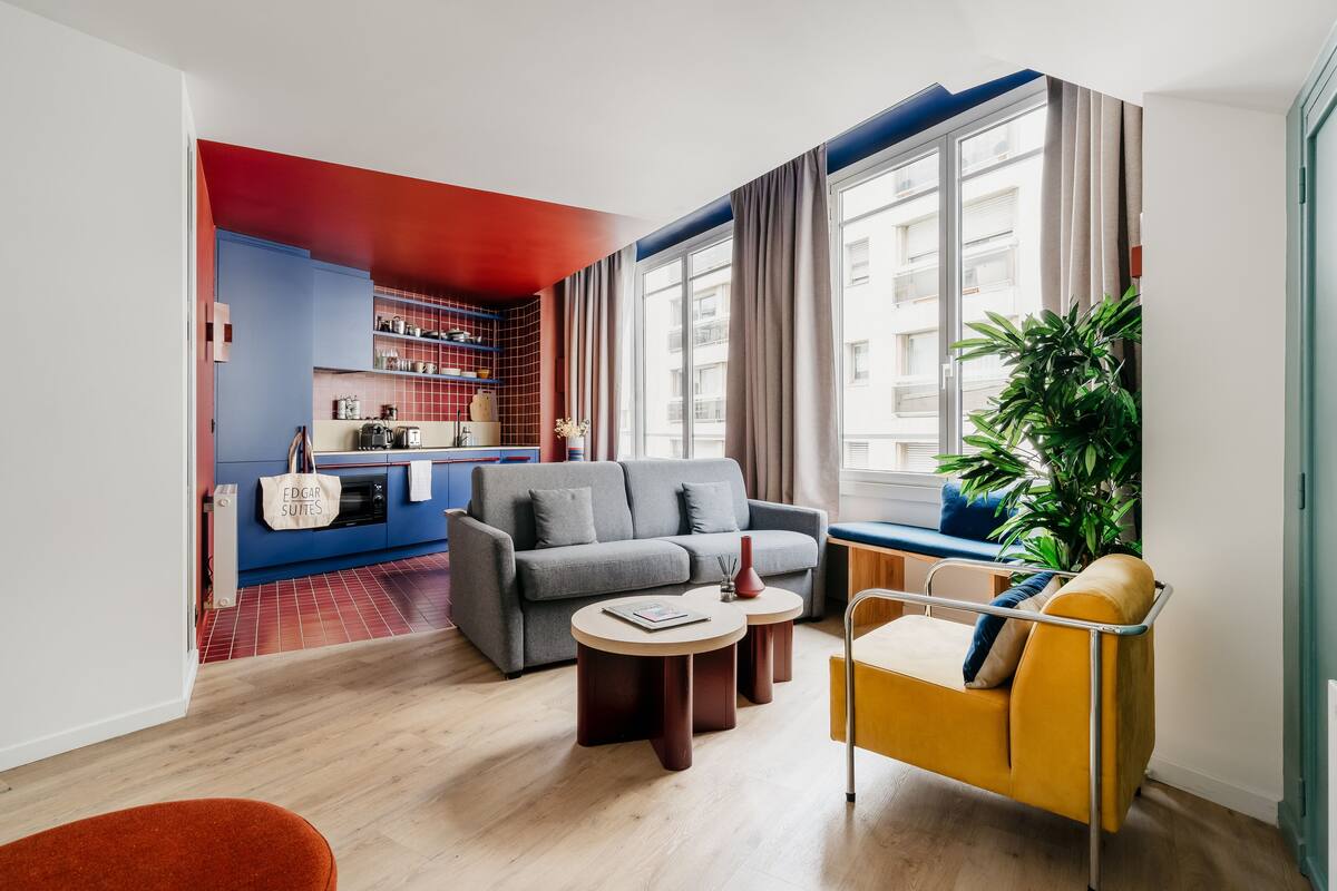 Una sala de estar moderna con un sofá, dos mesitas auxiliares, un sillón amarillo y un ventanal con cortinas.