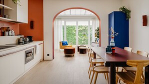 A modern kitchen with a dining area, featuring a large window, a dining table with chairs, and a kitchen counter with appliances.