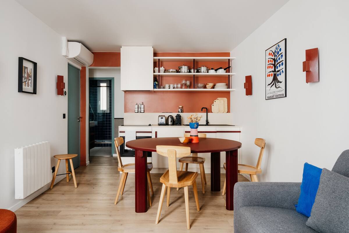 Una cocina moderna con armarios blancos, una mesa de comedor con sillas de madera y un sofá gris con un cojín azul.