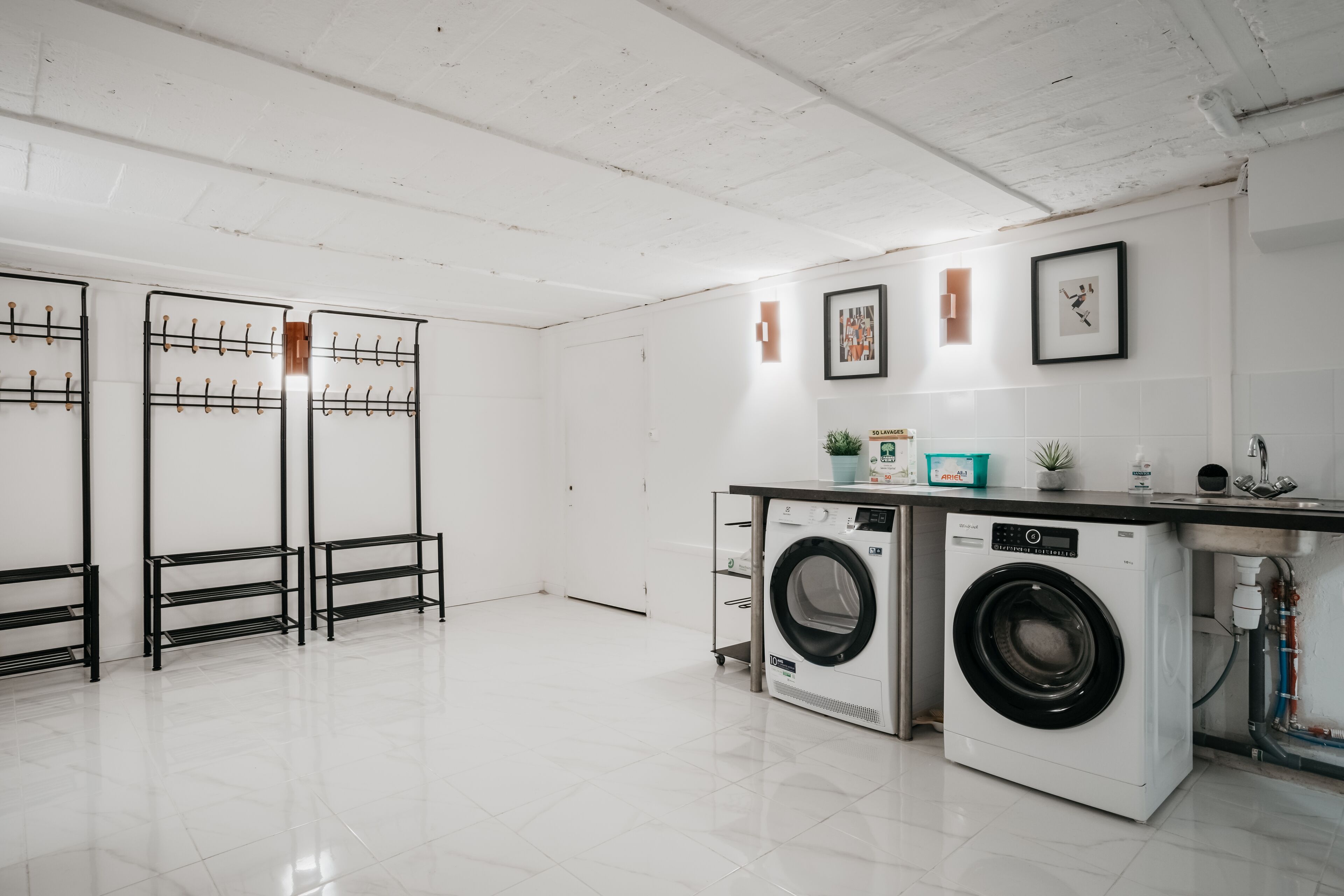 A laundry room with two washing machines, a sink, and a countertop with a plant and a picture frame.