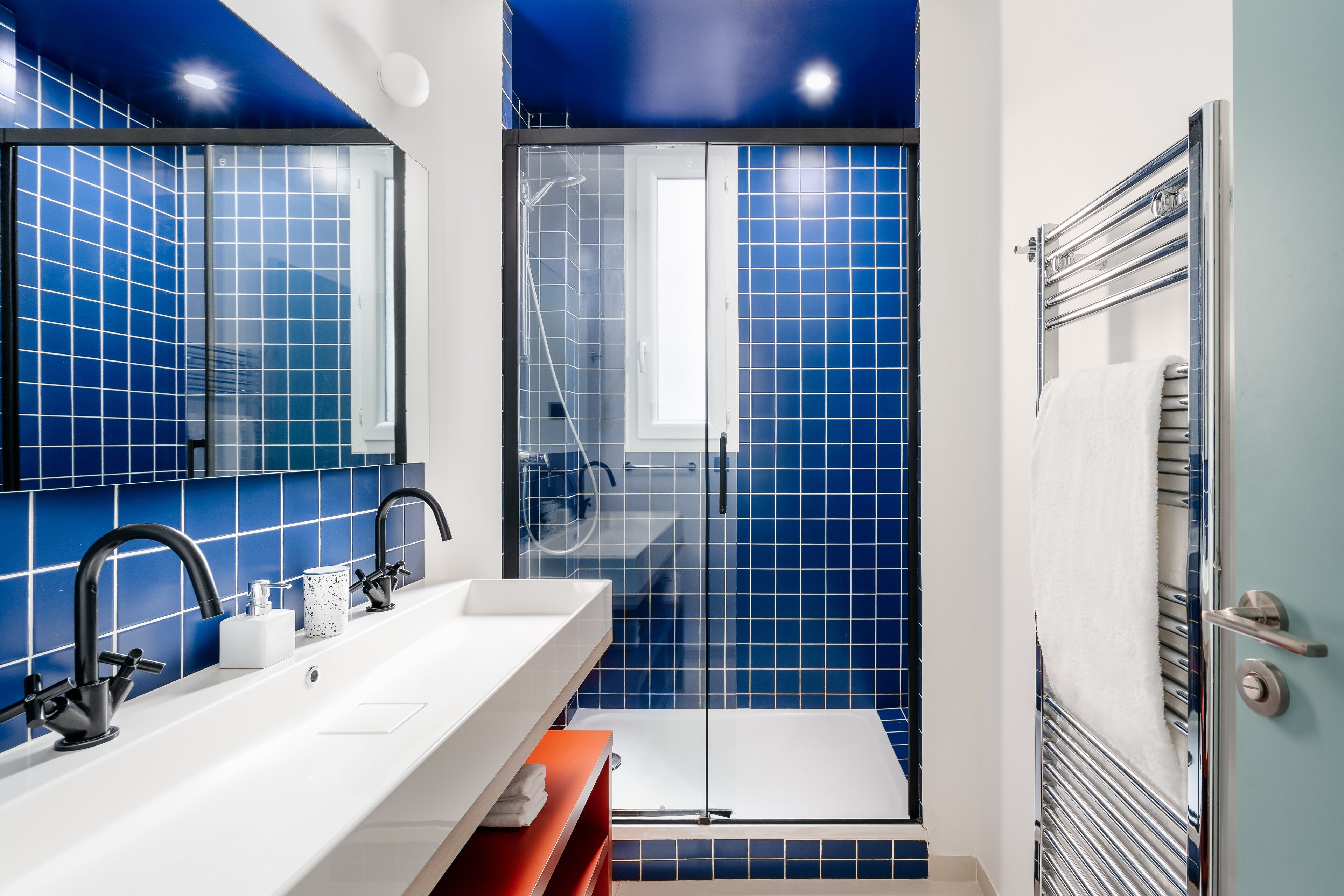 Un baño moderno con azulejos azules, un lavabo blanco y una cabina de ducha de vidrio.