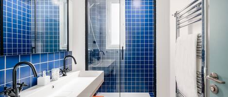 Un baño moderno con azulejos azules, un lavabo blanco y una cabina de ducha de vidrio.