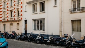 A row of parked scooters and a blue car on a city street.