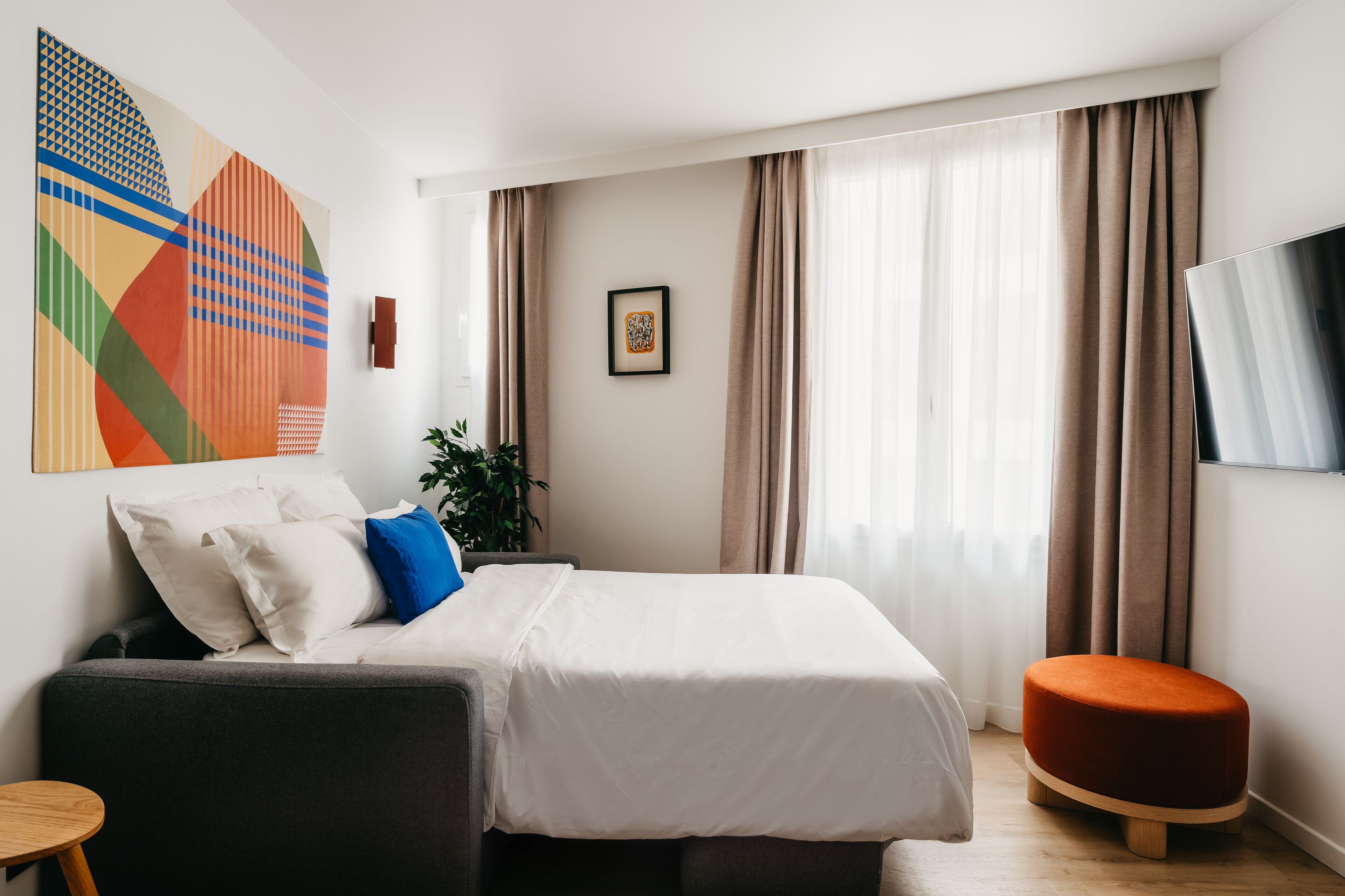 Une chambre d’hôtel moderne, équipée d’un lit, d’un canapé, d’une télévision et ornée d’un grand tableau abstrait au mur.