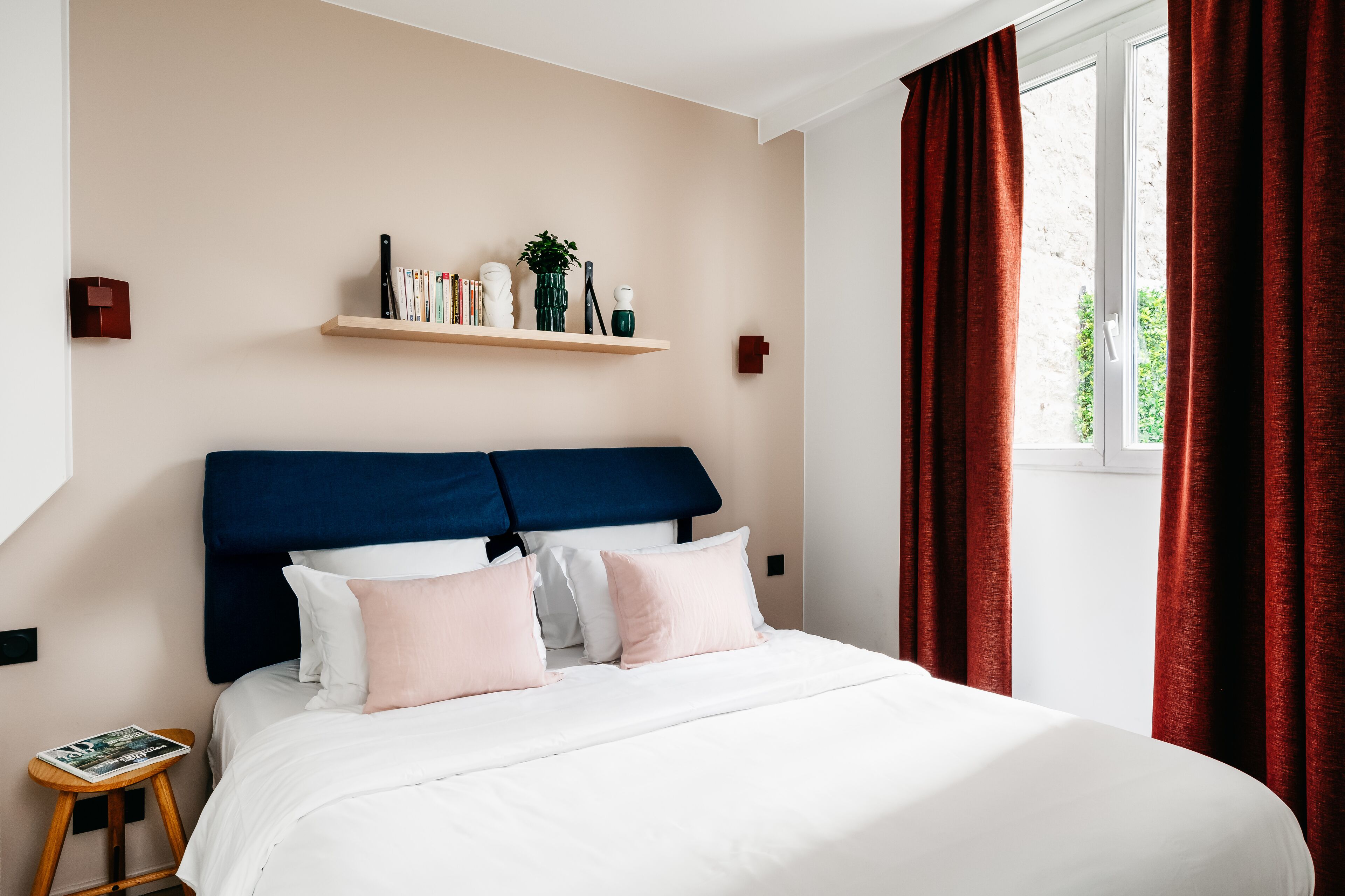 A neatly made bed with white and pink bedding, a blue headboard, and a wooden nightstand with a magazine.