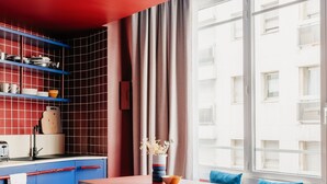A modern kitchen with red tiles, blue cabinets, and a wooden dining table with blue cushions.