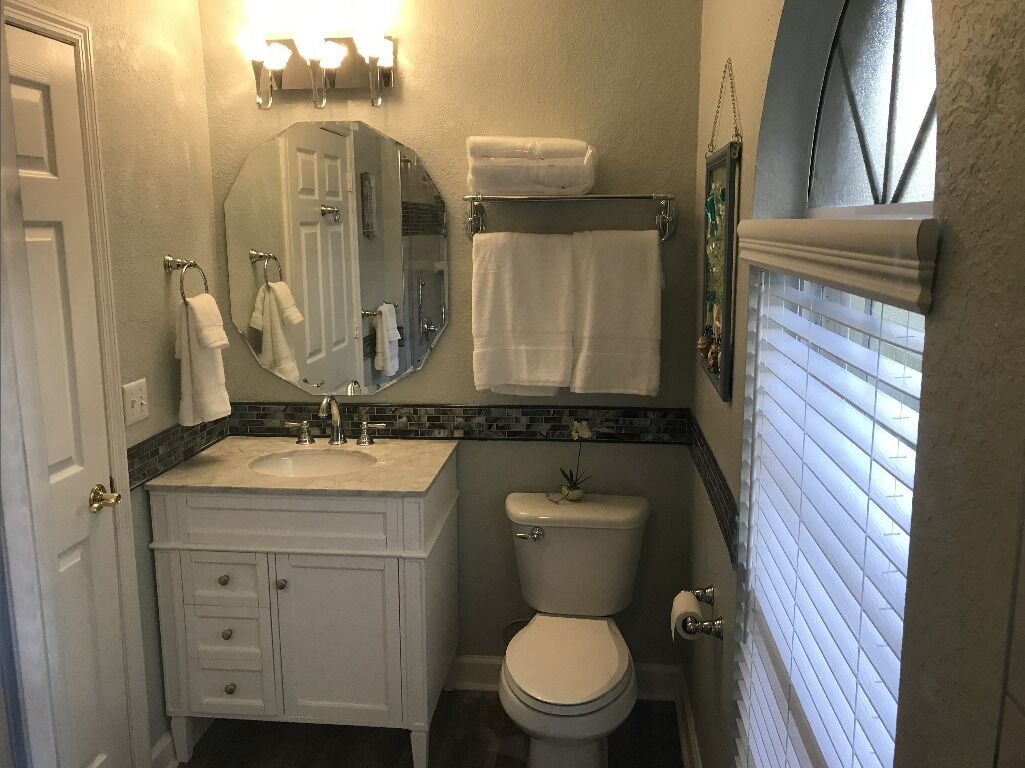 Un baño con lavamanos blanco, inodoro, espejo y toallero.