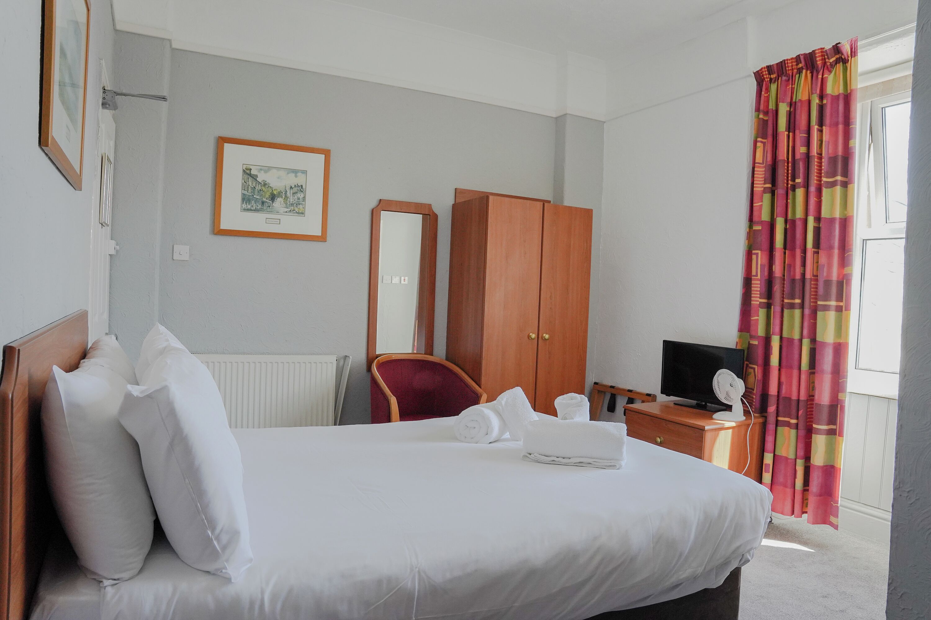 Une chambre d’hôtel comprenant un lit, une armoire en bois, une chaise, un téléviseur et une fenêtre avec des rideaux.