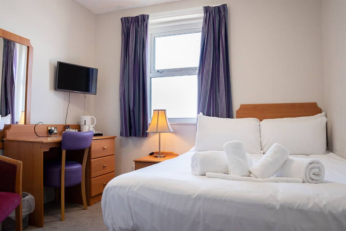 A hotel room with a bed, a desk, a chair, a television, and a window with curtains.