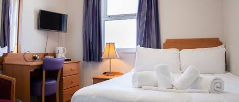 A hotel room with a bed, a desk, a chair, a television, and a window with curtains.