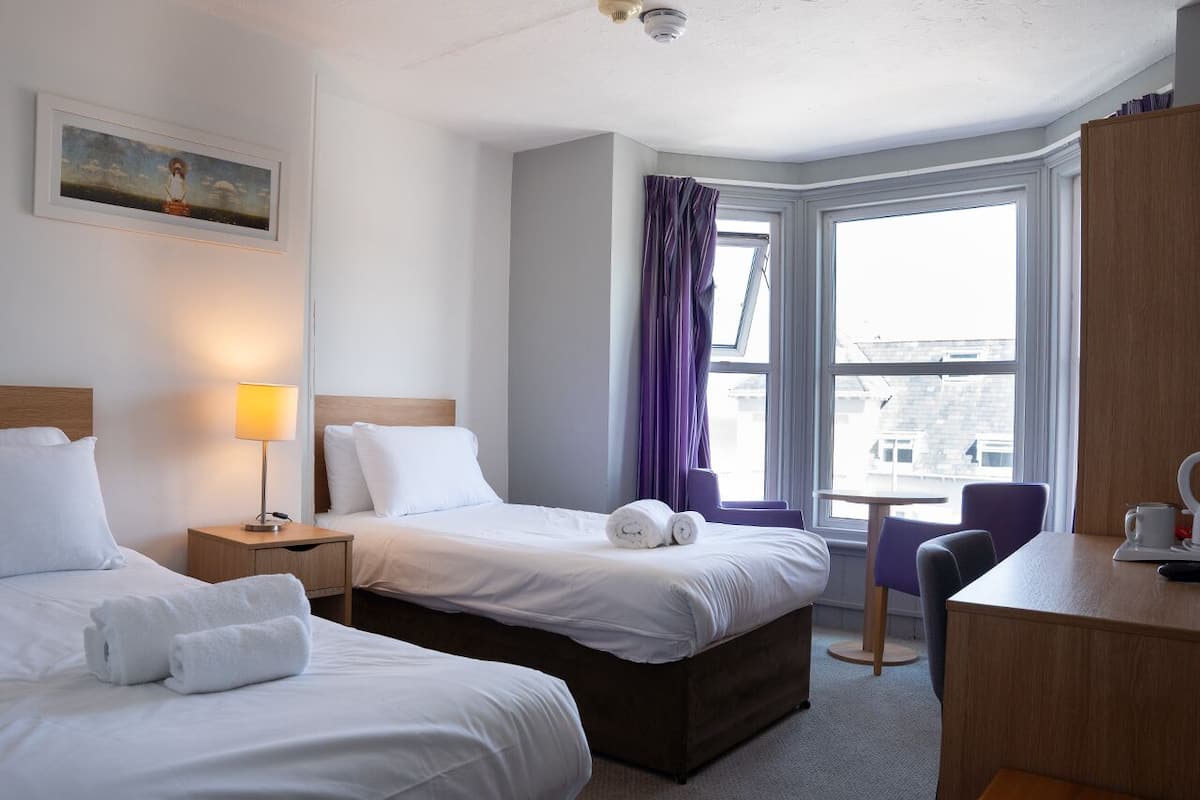 A hotel room with two beds, a desk, and a window with curtains.