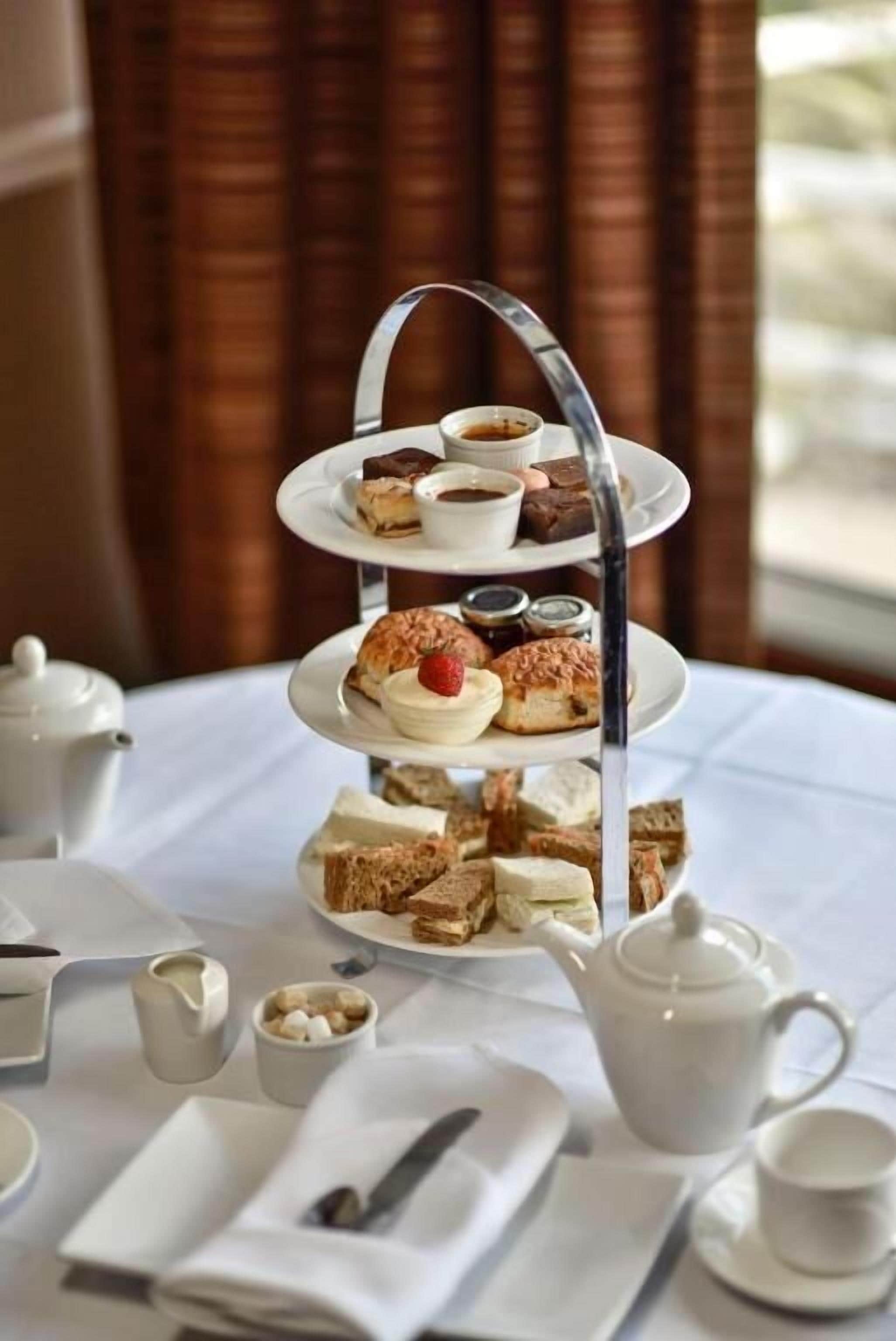 A three-tiered dessert stand with various pastries and a teapot on a table.