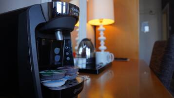 A coffee maker on a table with a lamp and a cup in the background.