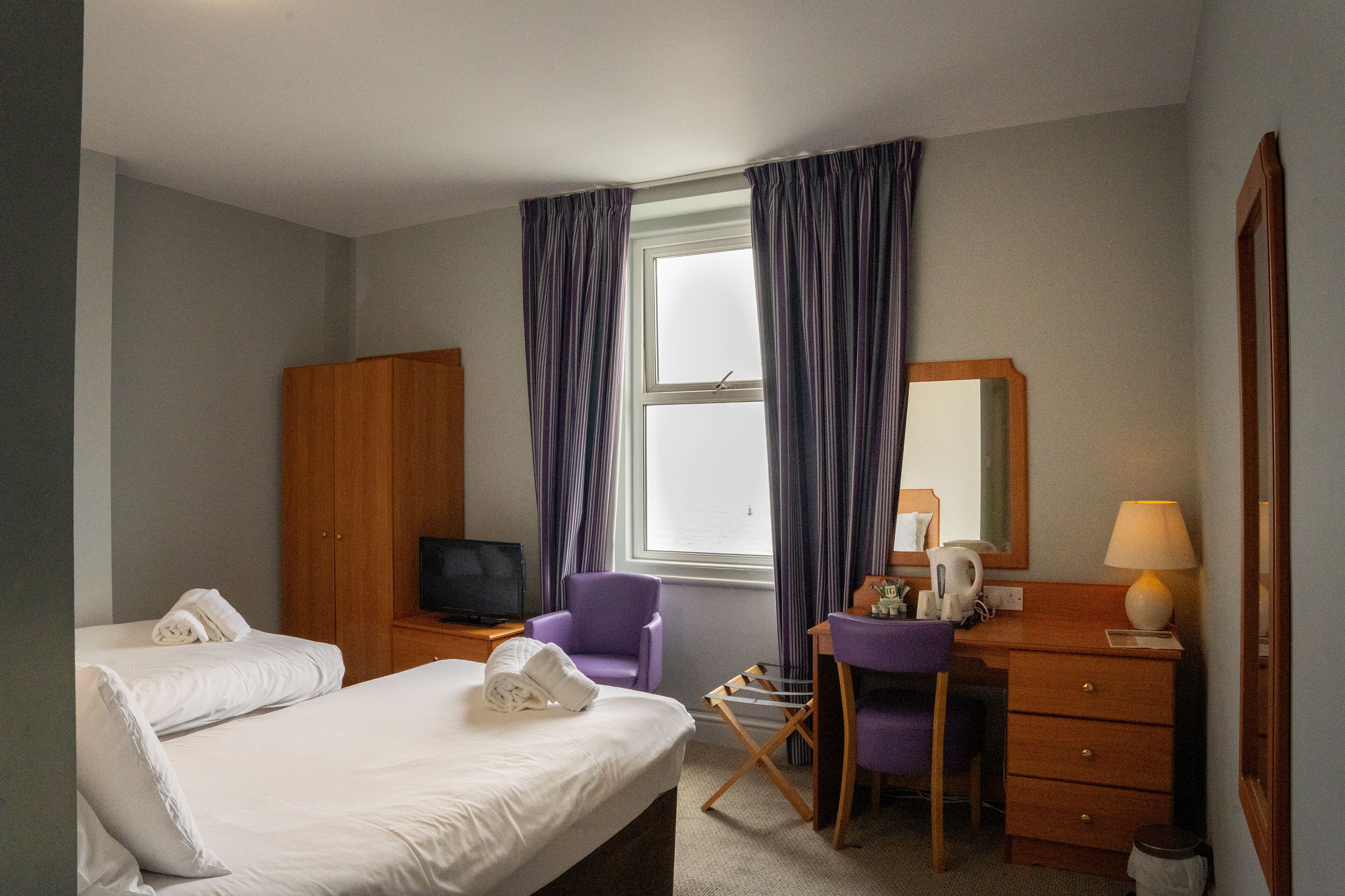 Une chambre d’hôtel équipée d’un lit, d’un bureau, d’une chaise, d’une télévision, d’une lampe et d’une armoire.