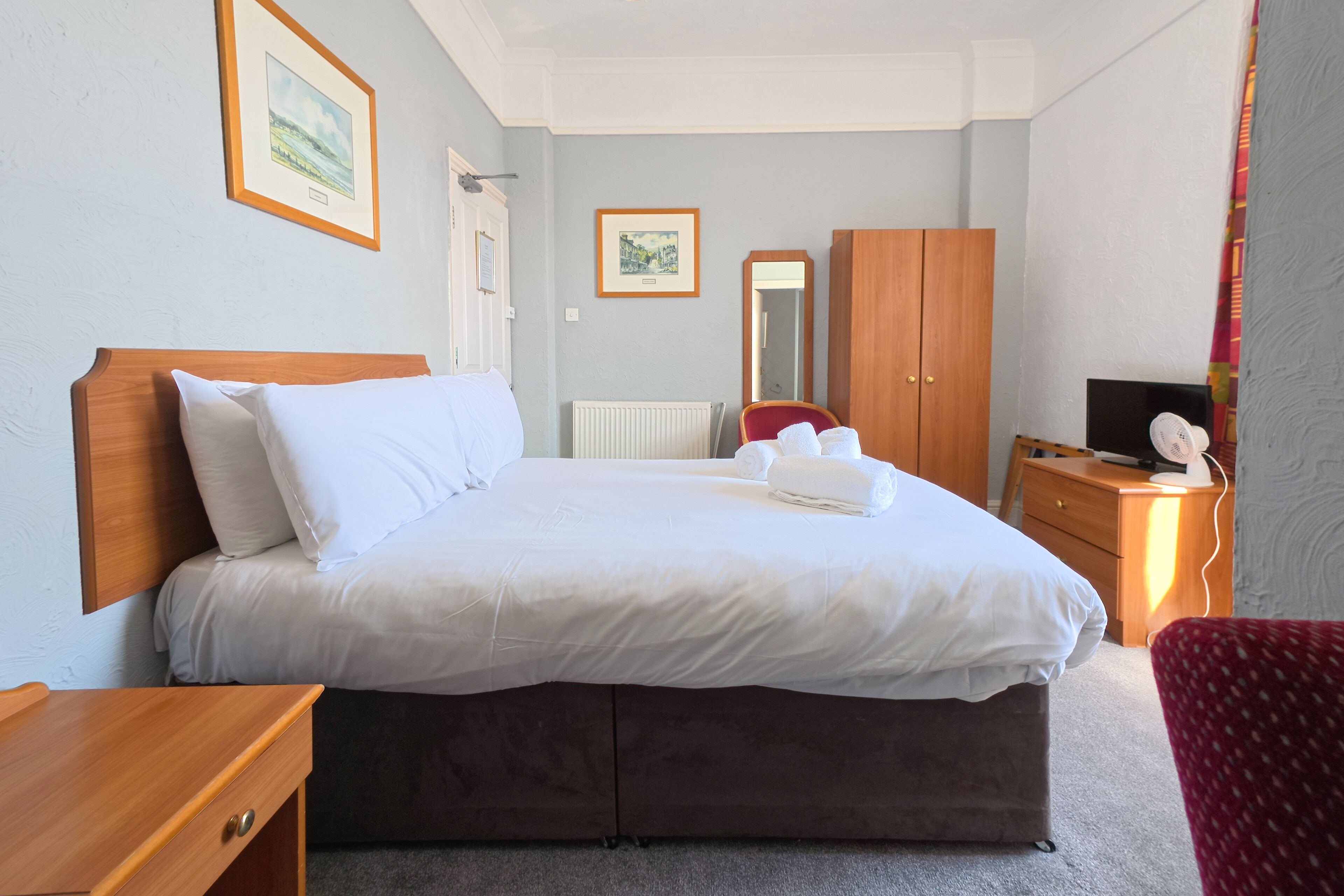 A neatly made bed with white linens, a wooden headboard, and a wooden nightstand with a lamp.