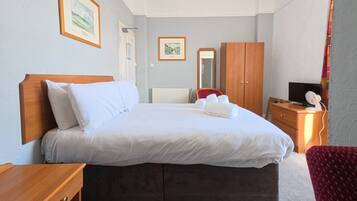 A neatly made bed with white linens, a wooden headboard, and a wooden nightstand with a lamp.