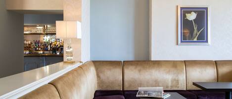 A modern lounge area with a sofa and a table, a bar in the background, and a framed picture on the wall.