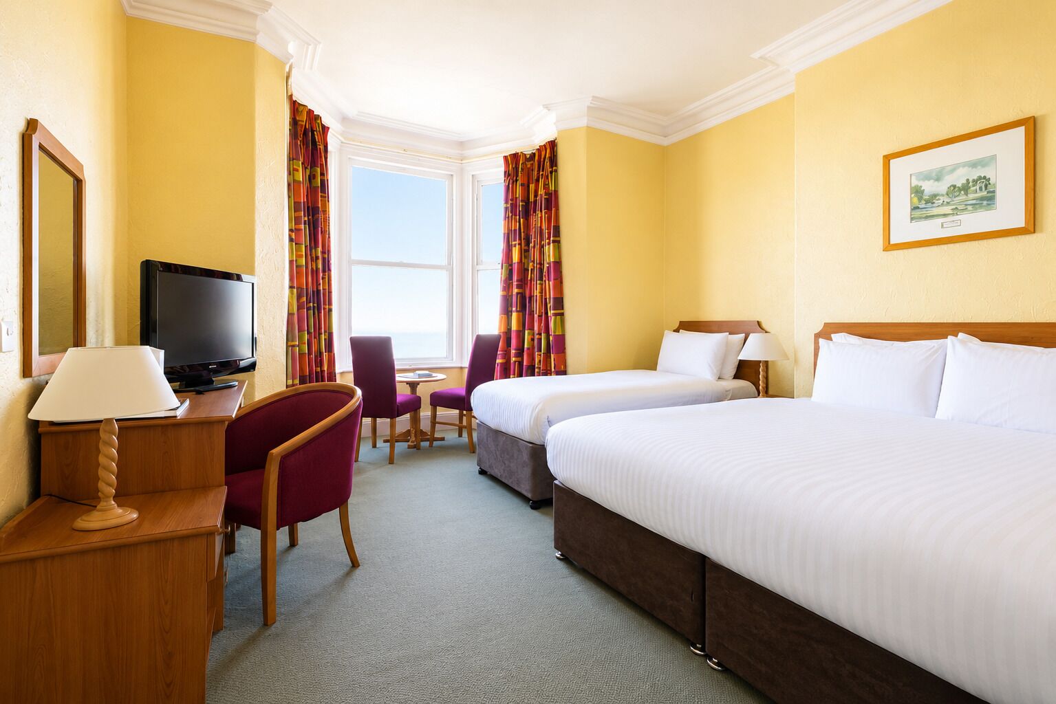 A hotel room with two beds, a TV, a desk with a lamp, a chair, and a window with curtains.
