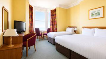 A hotel room with two beds, a TV, a desk with a lamp, a chair, and a window with curtains.