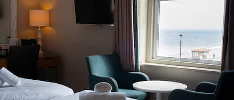 Une chambre d’hôtel avec deux lits, une télévision, une chaise, une table et une vue sur la mer.