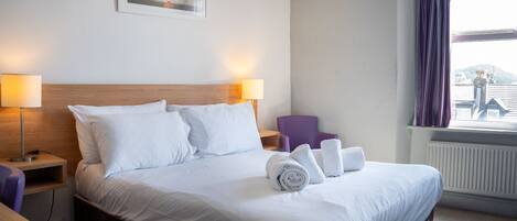 Een hotelkamer met een groot bed, twee bedlampen, een stoel en een raam met gordijnen.